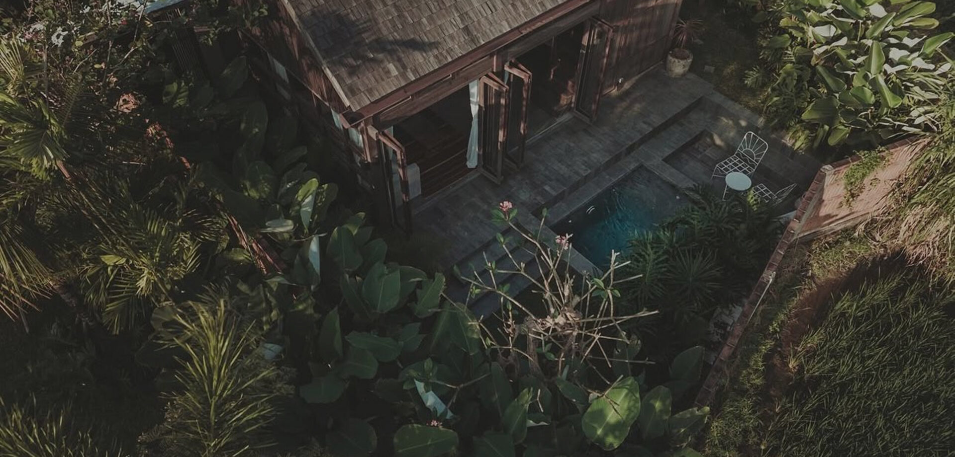 Aerial view of a timber-clad villa and small pool set among dense tropical greenery