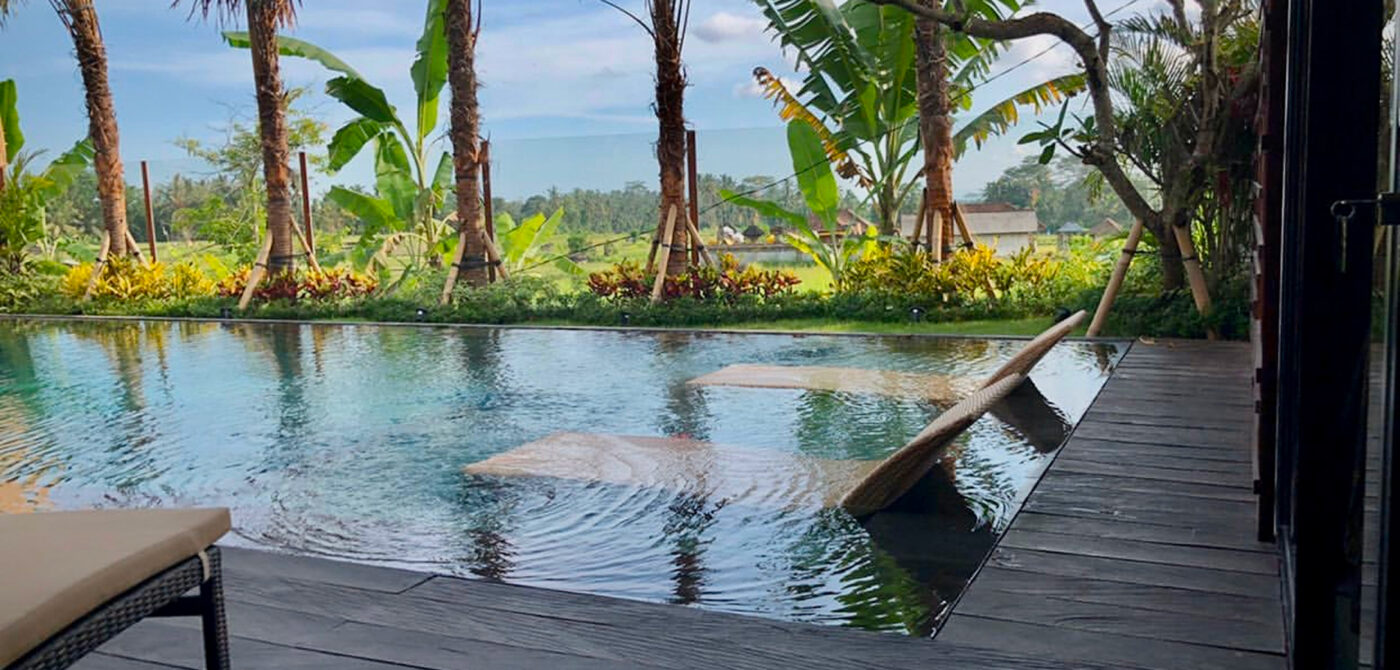 Hardwood pool deck beside an infinity pool with palms and Bali rice-field views
