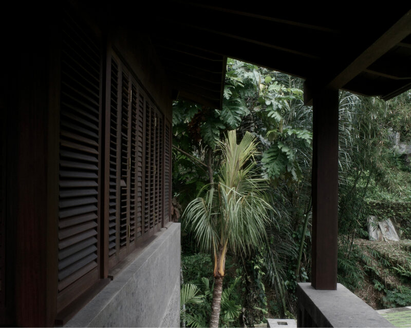 Timber villa veranda with louvered wood shutters and posts beside tropical plants