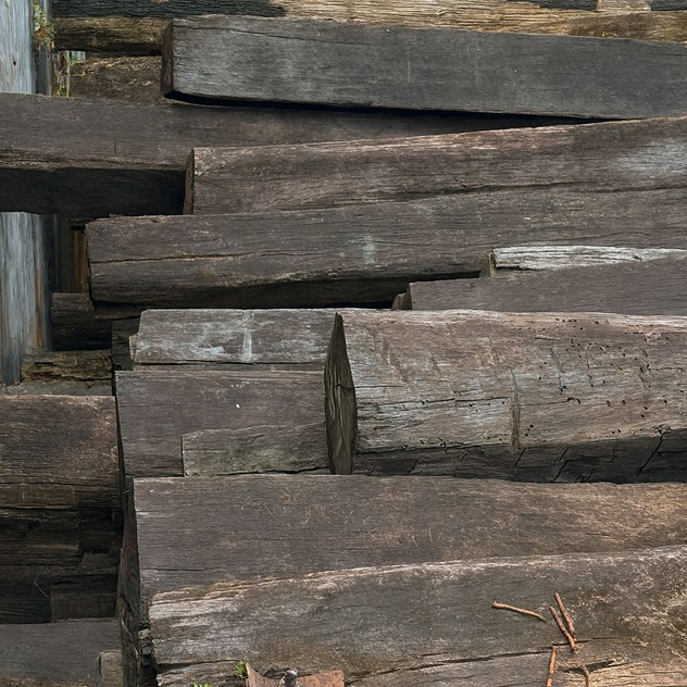 Stack of weathered grey reclaimed Ulin ironwood beams with rough sawn faces and split grain