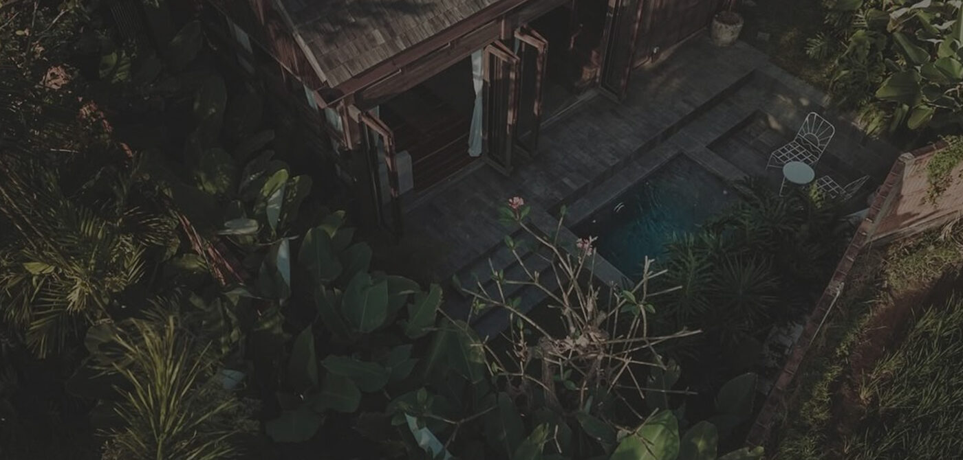 Aerial view of a dark timber Bali villa with a thatched roof and plunge pool framed by foliage