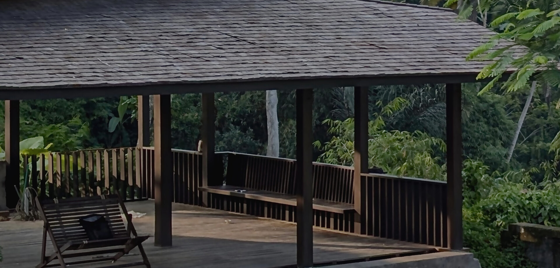 Open-sided timber pavilion with a shingled roof and hardwood deck overlooking lush jungle
