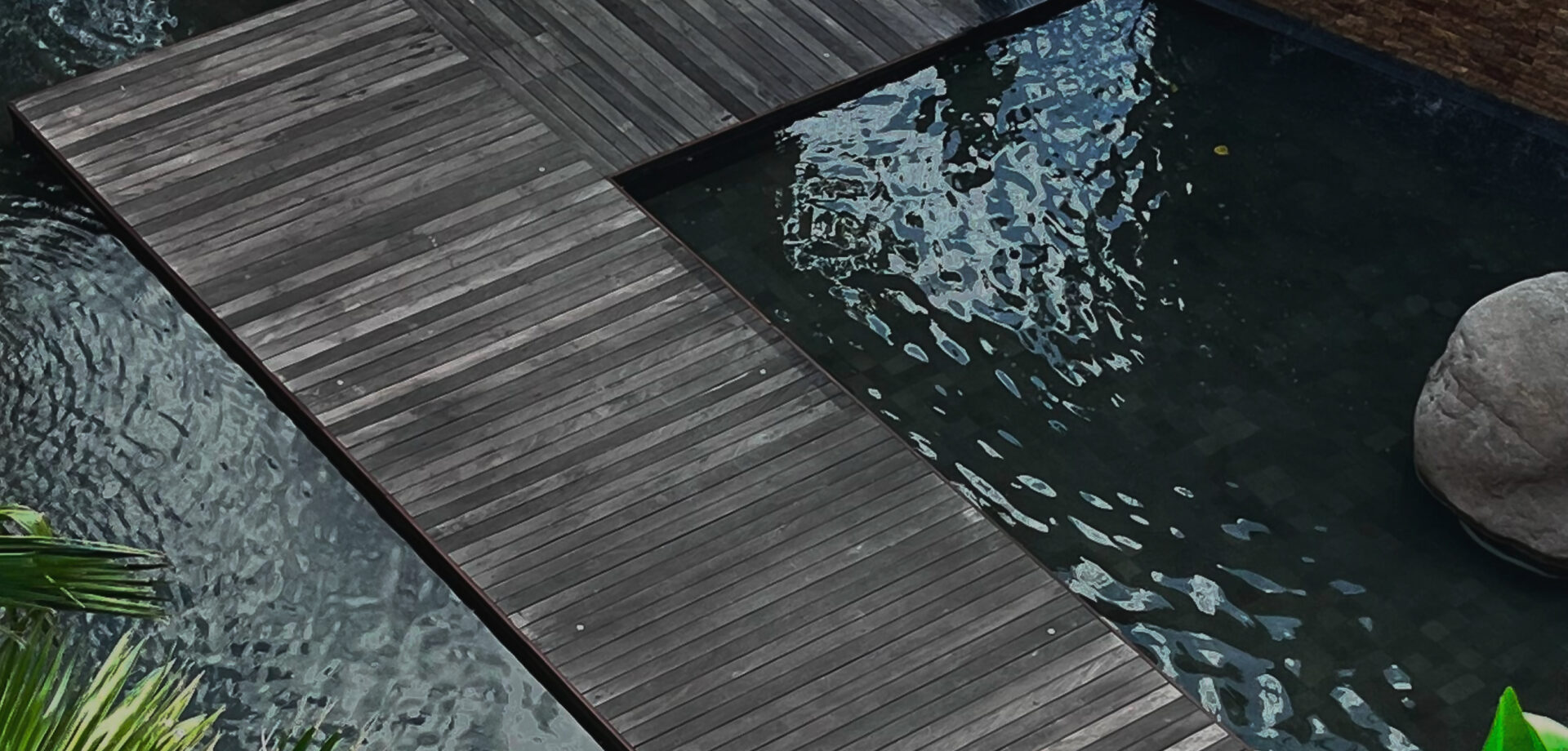 Grey hardwood pool deck with a timber walkway crossing a koi pond, viewed from above