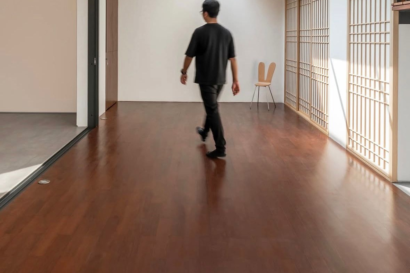 Man walking across glossy deep-brown solid wood flooring in a bright minimalist room with timber screens