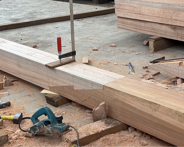 Squared hardwood timber beam clamped at a joint in an open-air woodworking workshop