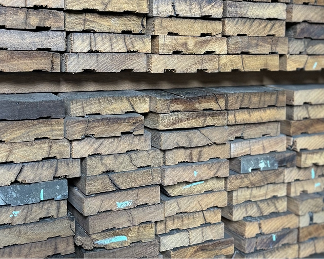 Rows of rough-sawn dark tropical hardwood boards stacked and seen end-on