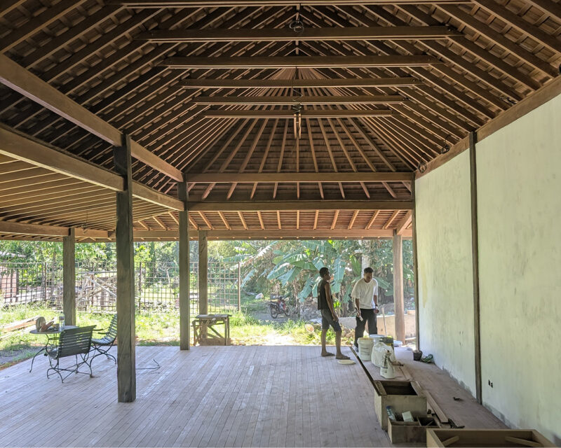 Open-sided pavilion under construction showing an exposed timber roof frame and plank floor