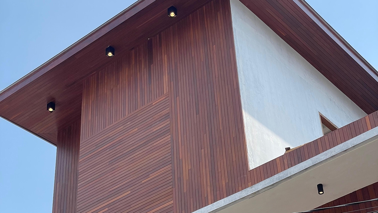 Underside of a building eave clad in rich reddish-brown timber slats with recessed downlights