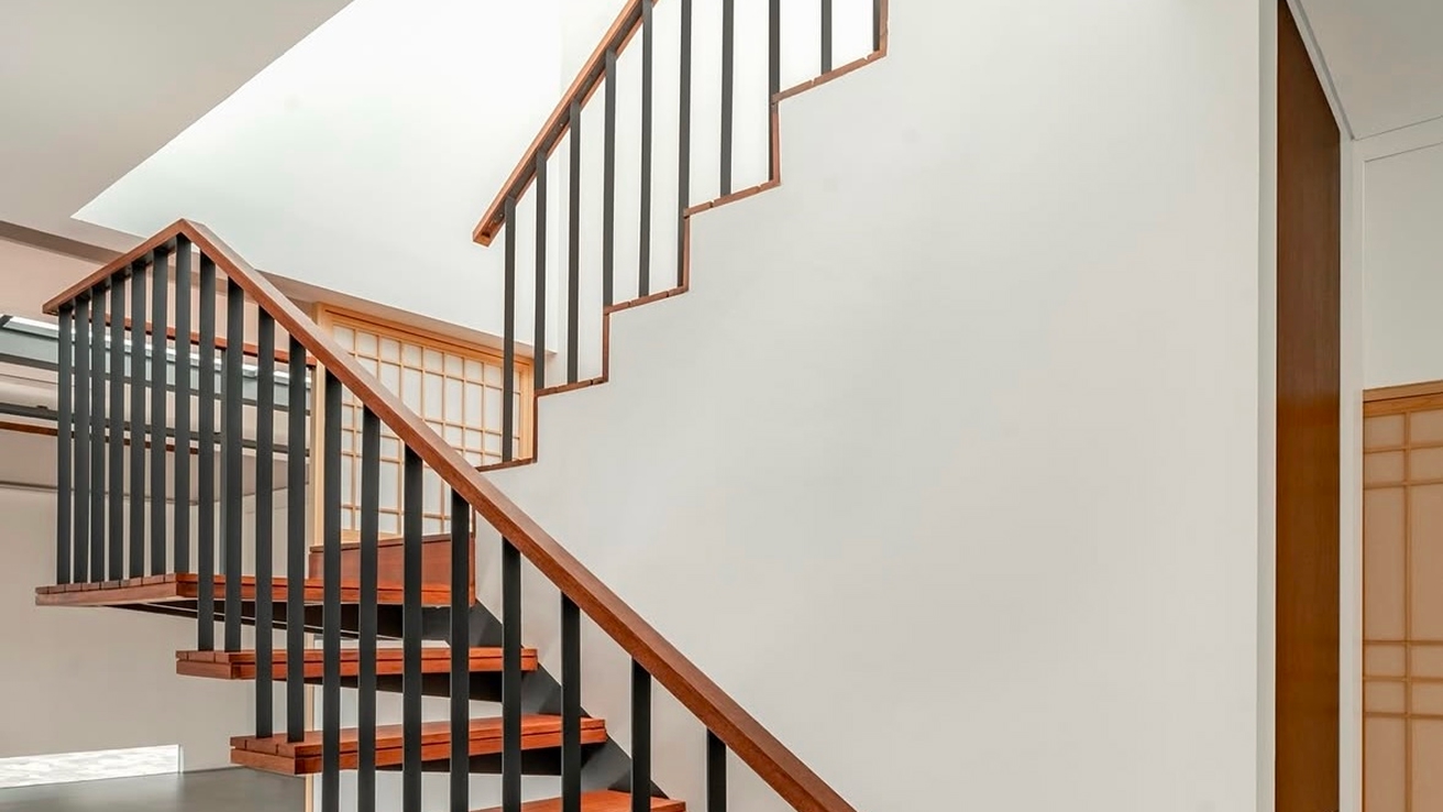 Floating staircase with reddish-brown hardwood treads, a black steel stringer and slim balusters