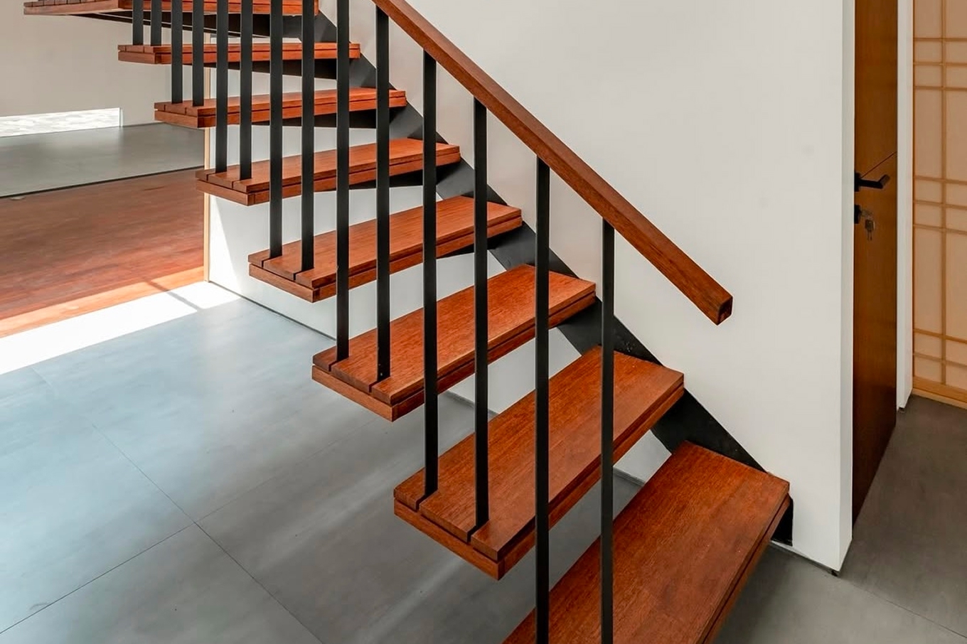 Cantilevered hardwood stair treads in warm reddish tones with black metal balusters on a white wall