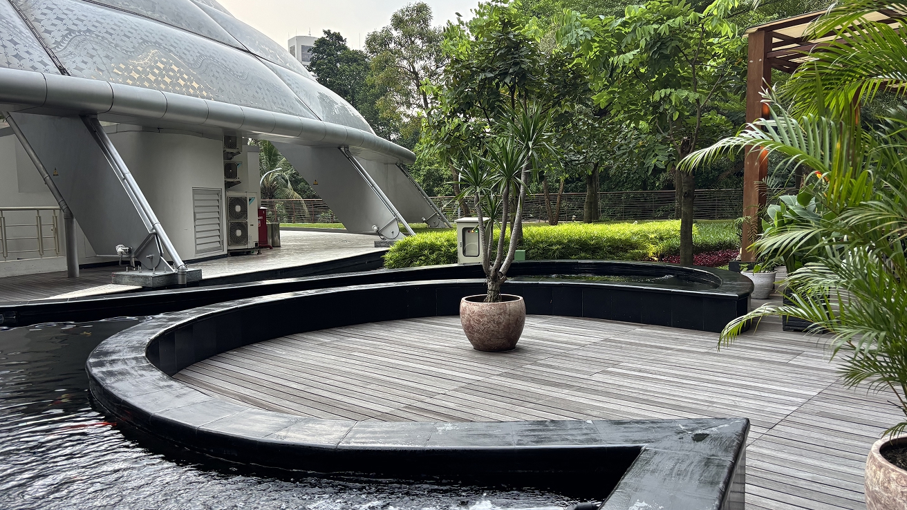 Smooth grey hardwood deck curving around a planter beside a domed glass pavilion