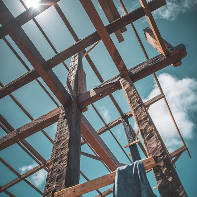 Looking up at a heavy timber roof frame of rough-hewn reclaimed hardwood beams against blue sky