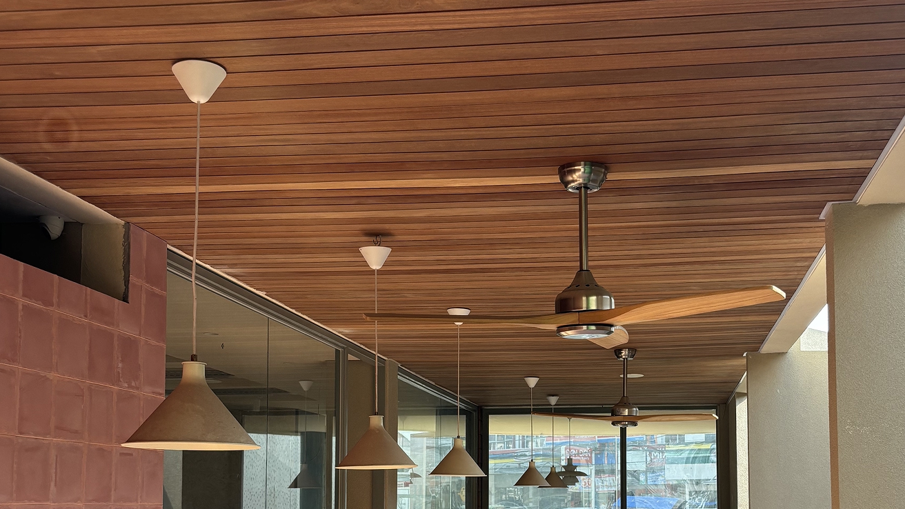 Reddish-brown timber slat ceiling on a covered shopfront terrace with pendant lights and a fan