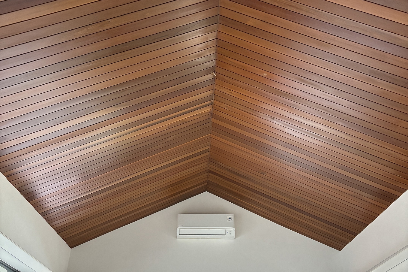 Reddish-brown timber ceiling slats lining a vaulted ceiling meeting at a central ridge